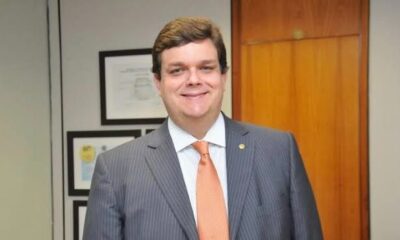 Wolney Queiroz em um escritório, analisando documentos sobre Previdência Social, com cidade ao fundo.