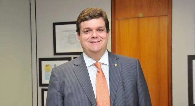 Wolney Queiroz em um escritório, analisando documentos sobre Previdência Social, com cidade ao fundo.